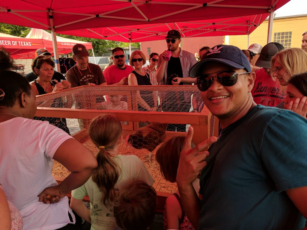 People gathered around a chicken coop, with one man holding up a victory sign and looking at the camera.