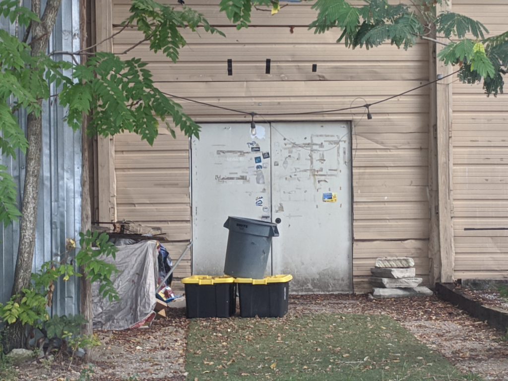 Entrance to the Museum of Human Achievement in Austin, featuring two white doors and brown leaves on the grass infront. 