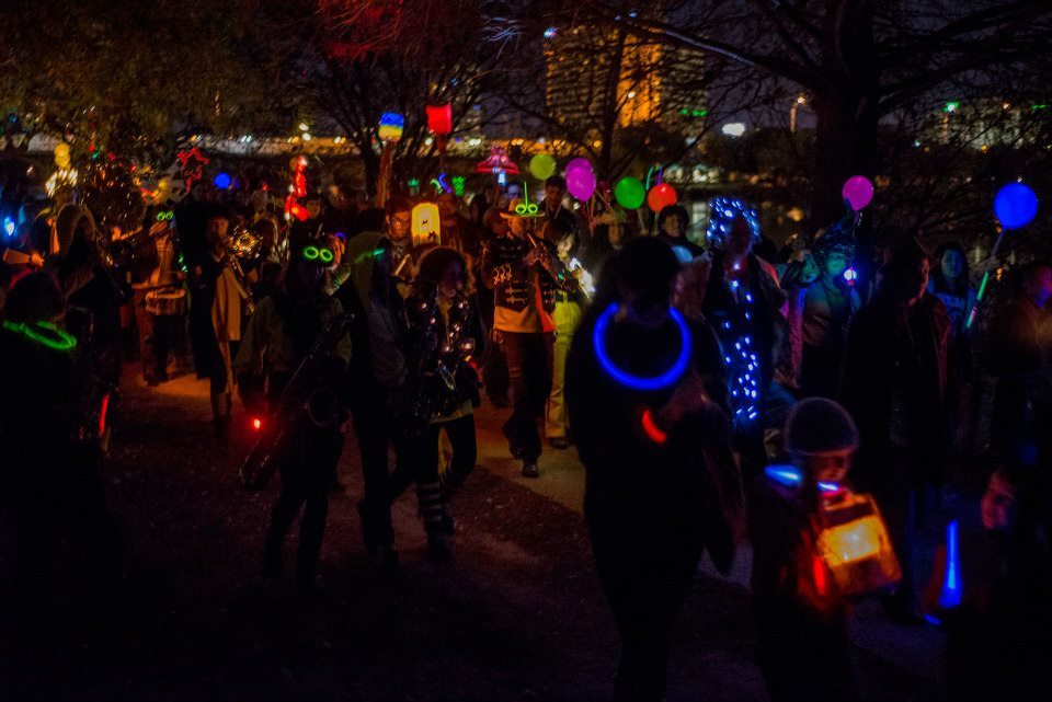 People wearing neon accessories walk alongside the Minor Mishap Marching Band players.