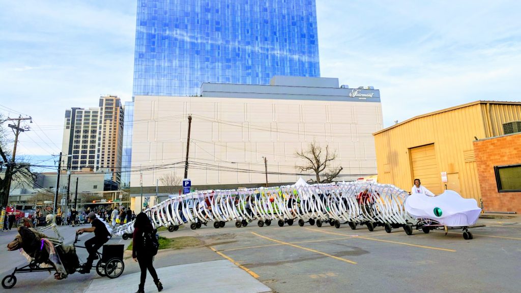 Two animal shaped bikes in a parking lot in Austin, including a long snake bike and a bike with a skeleton rider. 